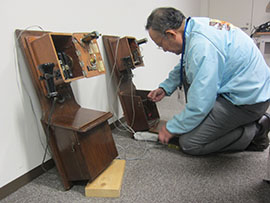 復元したデルビル磁石式電話の様子を見る中澤さんの写真